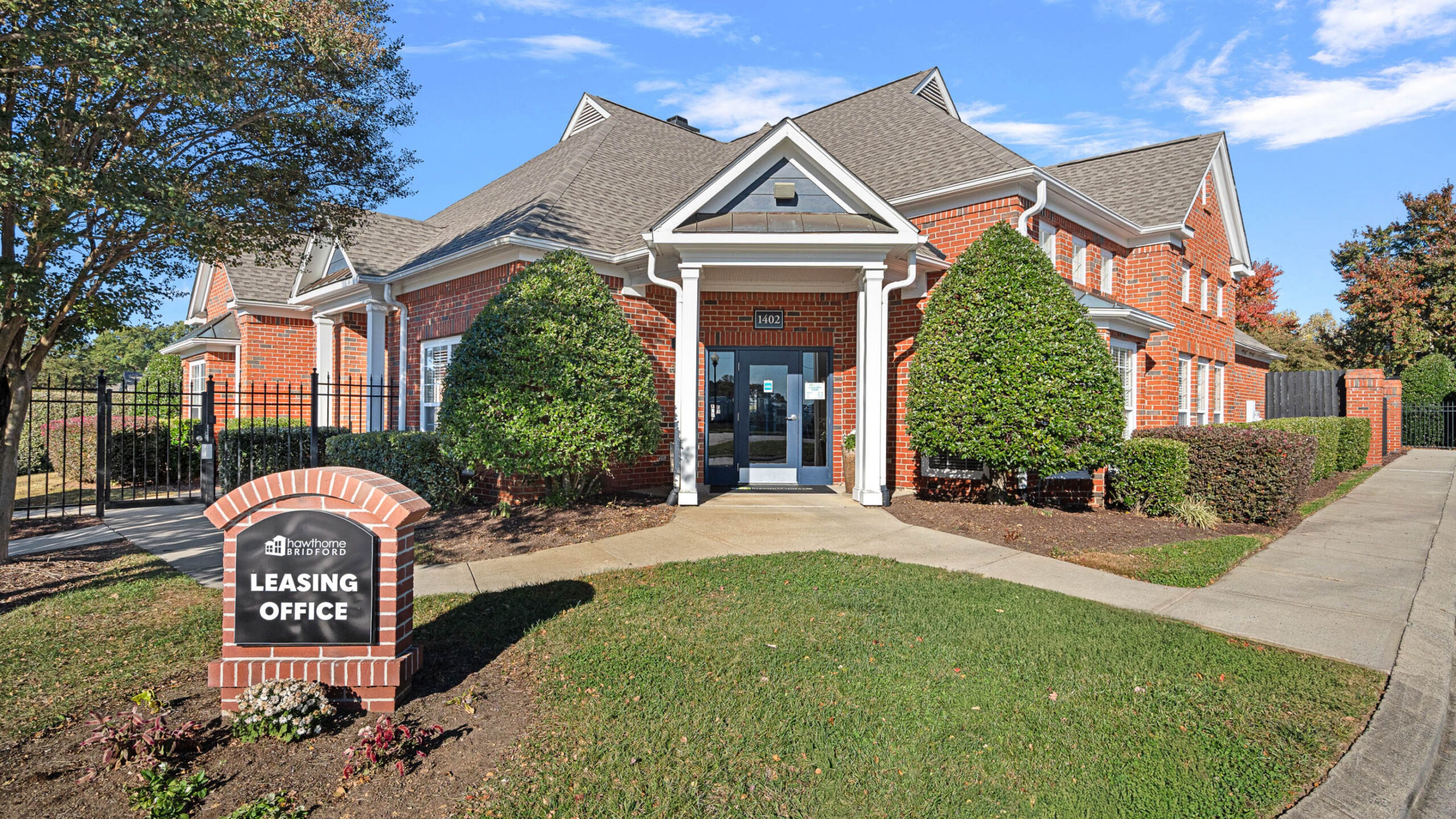 Red brick building with white trim, manicured bushes, and a "Leasing Office" sign in front.